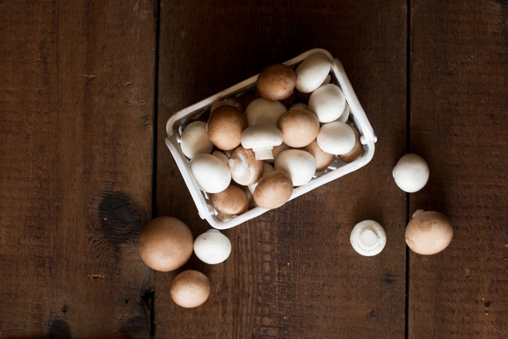 tray holding white and brown mushrooms on wooden table